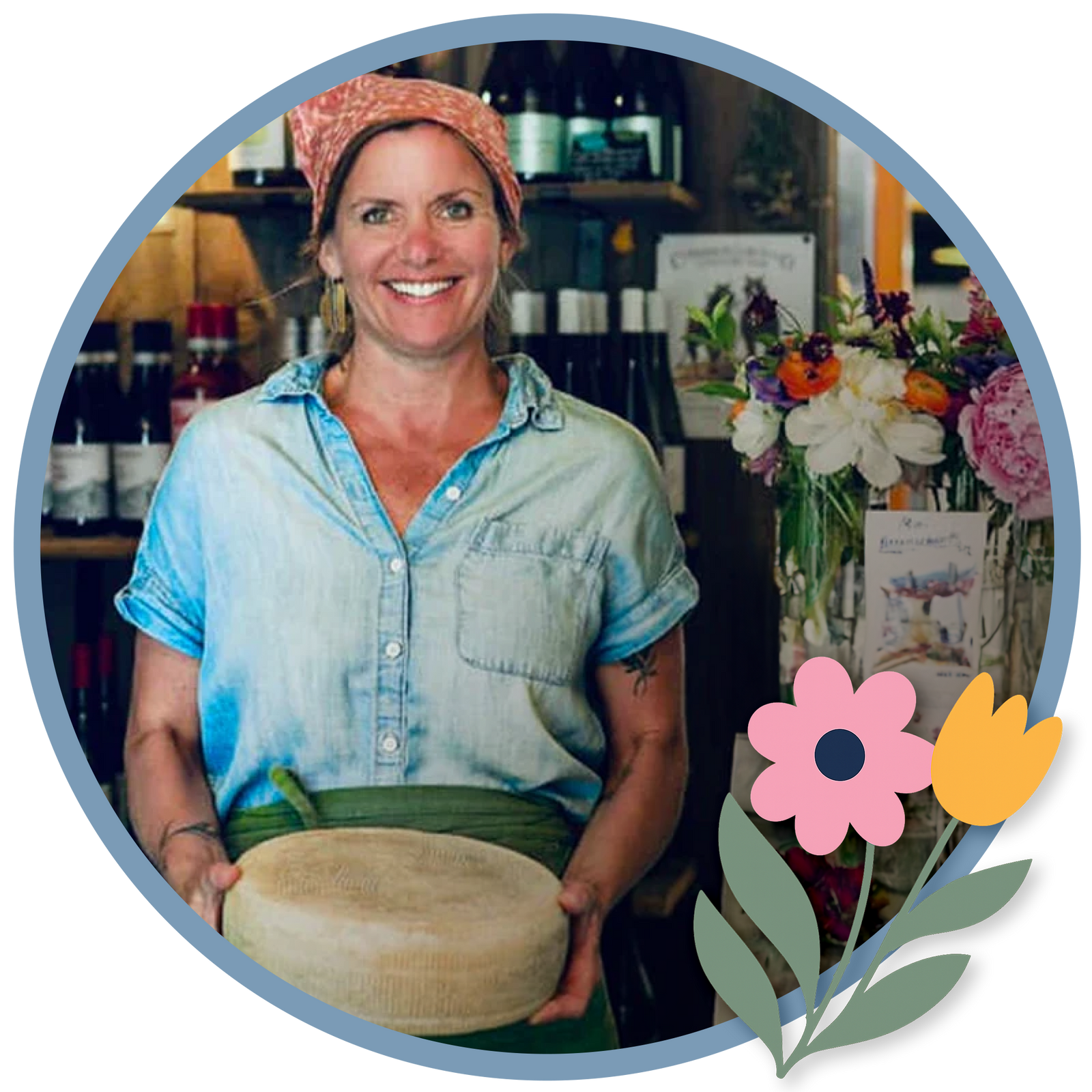 Amy from Crooked Face Creamery holding a wheel of cheese with spring floral accents in the creamery shop