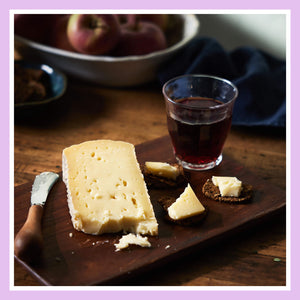 Cheese wedge served with a glass of cider and rustic setting